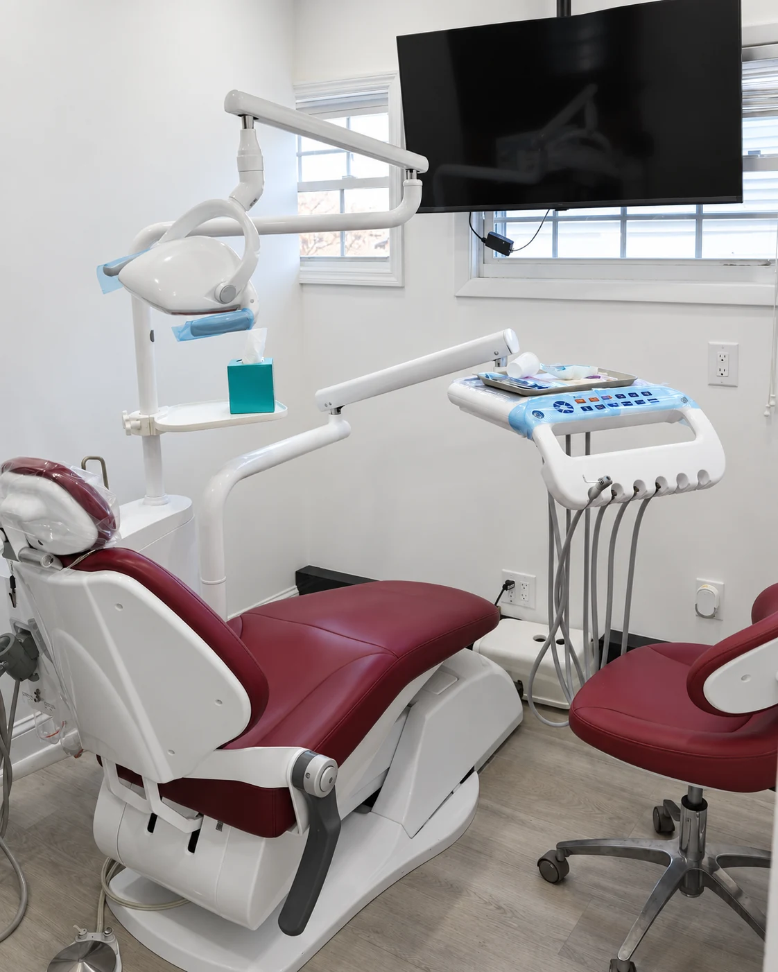 Burgundy dental chair, examination light and wall monitor in a Bellerose treatment room